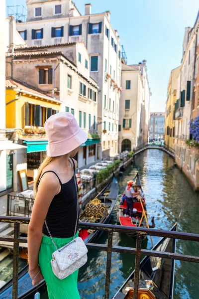 Venedik gondol kanalına hayran genç bir turist. Yaz kıyafeti giymiş bir kadın yolcu köprüde duruyor ve İtalya Venedik 'te büyüleyici bir kanaldan gondolların geçişini izliyor.