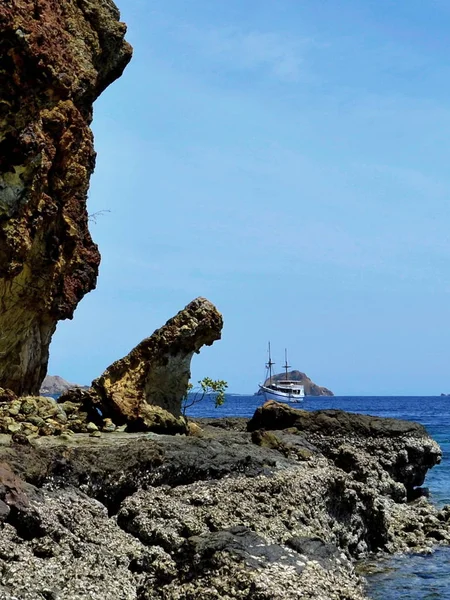 A small ship in the sea on a background of rocky reefs. — Stock Photo, Image