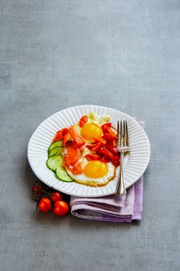 Sabah kahvaltı tabağı somon füme, sahanda yumurta, domates ve salatalık ile açık beton renkli yan görünüm üzerinde yakın çekim. İyi yağlar sağlıklı beslenme kavramı.
