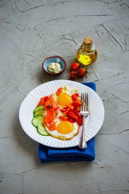 Sabah kahvaltı beyaz tabak kapatın. Som balığı, kızarmış yumurta, domates ve salatalık açık beton renkli üstten görünüm üzerinde füme. İyi yağlar sağlıklı beslenme kavramı. Düz yatıyordu stili.