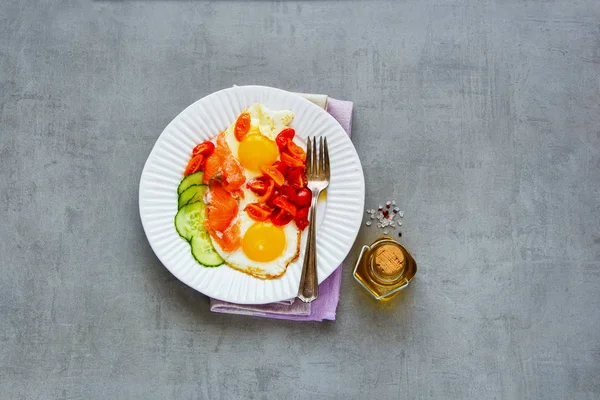 Somon füme, sahanda yumurta, domates ve salatalık üzerinde açık beton renkli üstten görünüm ile lezzetli sabah kahvaltı tabağı. İyi yağlar sağlıklı beslenme kavramı. Düz yatıyordu stili.