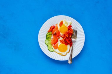 Parlak mavi zemin üzerine plaka sabah kahvaltı. Füme somon, kızarmış yumurta, domates ve salatalık. İyi yağlar sağlıklı beslenme kavramı. Düz yatıyordu tarzı. Üstten görünüm
