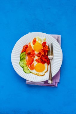 Parlak mavi arka plan düz tabağa taze sabah odaya yatıyordu. Füme somon, kızarmış yumurta, domates ve salatalık. İyi yağlar sağlıklı beslenme kavramı. Üstten görünüm