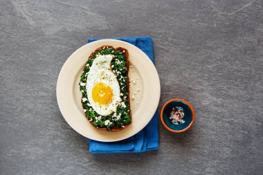 Delicious breakfast rye bread sandwich in plate with kale, fried egg and feta cheese on concrete background top view. Healthy eating, slimming, diet lifestyle concept. Flat lay style. clipart