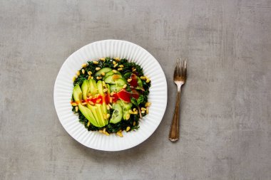 Yeşil vegan salata plaka kale, avokado, salatalık, çam fıstığı ve açık beton renkli üstten görünüm üzerinde giyinme tatlım. Sağlıklı yeme, zayıflama, diyet, vegan gıda kavramı. Düz yatıyordu stili.