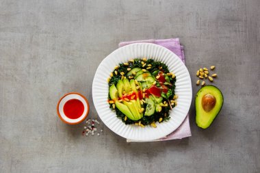Düz-lay yeşil vegan salatası kale, avokado, salatalık, çam fıstığı ve açık beton renkli üstten görünüm üzerinde giyinme tatlım. Sağlıklı yeme, zayıflama, diyet, vegan gıda kavramı. 