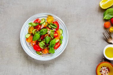 Arka plan düz lay organik maddeler ve ışık üzerinde sağlıklı salata tabağı. Kiraz renkli domates, salatalık, kırmızı soğan, zeytin yağı, limon, fesleğen ve baharat yukarıdan.