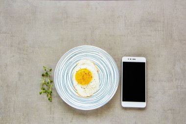 Plaka ve smartphone düz-lay kızarmış yumurta kahvaltı. Eve geri kalan ara natürmort ışık taş zemin, üstten görünüm.