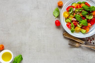 Düz sağlıklı salata tabağı ve maddeler ışık arka plan üzerinde yatıyordu. Kiraz renkli domates, salatalık, kırmızı soğan, zeytin yağı, fesleğen ve baharat görünümü top.