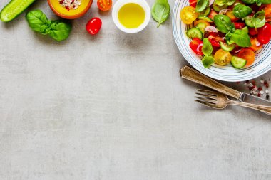 Sağlıklı salata tabağı ve yukarıdan ışık arka plan üzerinde taze malzemeler. Cherry domates, salatalık, kırmızı soğan, zeytin yağı, fesleğen ve baharat düz-lay.