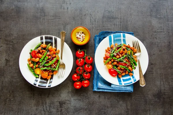 Beans salad plates with aspargus, micro greens and tomatoes flat lay. Vegan healthy energy boosting salad on dark background. Clean eating, superfood, vegan, detox food concept. Top view