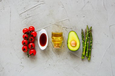 Kiraz domates, zeytin yağı, avokado ve aspargus düz soyunma yatıyordu. Sağlıklı gıda seçimi yeme temiz. Pişirme malzemeleri. Üstten görünüm. Açık renkli ham Bio yemek.