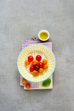 Düz salata malzemeleri yatıyordu. Kase, fesleğen ve zeytin yağı boşaltmak ile ışık arka plan üzerinde renkli domates. Üstten görünüm