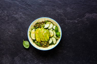 Sağlıklı yeşil yaz salatası kase kabak, salatalık, roka ve Avokado tohum ve siyah arka plan üzerine sos ile. Üstten görünüm, düz yatıyordu stili.