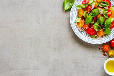 Düz malzemeler ve açık renkli taze salata tabağına yatıyordu. Kiraz renkli domates, salatalık, kırmızı soğan, zeytin yağı, fesleğen ve baharat yukarıdan.