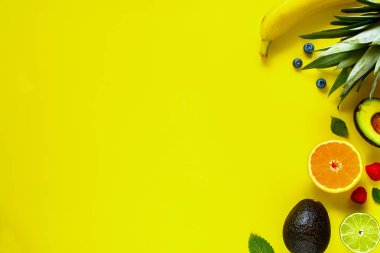 Organik tropikal meyve yapılmış yaratıcı düzeni. Düz lay-ananas, muz, portakal, limon, avokado, ahududu, yaban mersini sarı zemin üzerine. Gıda kavramı. Üstten görünüm