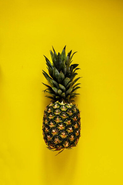 Flat lay of pineapple on yellow background. Tropical fruit from above. Useful natural organic food. One whole object. Style minimalist.