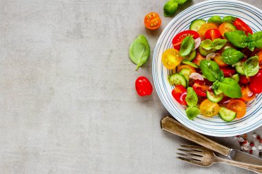Lezzetli sağlıklı salata tabağı ve malzemelerin ışık arka plan üzerine kapatın. Kiraz renkli domates, salatalık, kırmızı soğan, zeytin yağı, fesleğen ve baharat yatıyordu, en iyi görünüm düz.