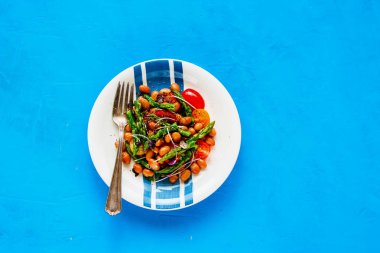 Mavi arka plan düz-lay Vegan salataya. Sağlıklı enerji artırma aspargus, mikro yeşillik ve domates ile plaka salata fasulye. Temiz beslenme, superfood, vegan, gıda kavramı detoks. Üstten görünüm
