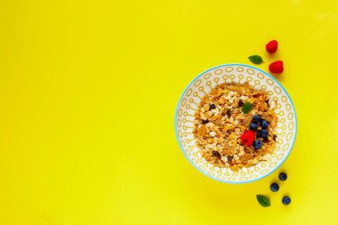 Müsli tabağı, taze meyveler ve nane yaprakları düz-lay. Sarı kopya alan arka plan üzerinde sağlıklı kahvaltı. Superfood ve detoks kavramı. Üstten görünüm