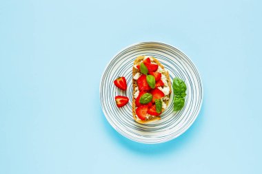 Sağlıklı kahvaltı veya aperatif kompozisyon. Ricotta peyniri, taze çilek ve fesleğen ile tam tahıl ekmeği, düz lay pastel açık mavi renkli bırakır. Yeme, Vejetaryen gıda kavramı temiz