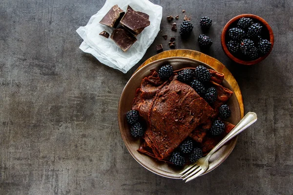 Flat-lay of chocolate crepes. Thin pancakes, chocolate bars and fresh blackberries