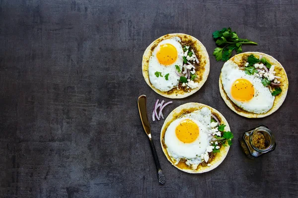 Flat-lay of healthy corn tortillas with fried eggs, pesto sauce and feta cheese