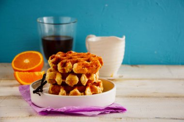 Belçika vanilya waffle, fincan kahve, turuncu ve mavi arka plan üzerinde akçaağaç şurubu