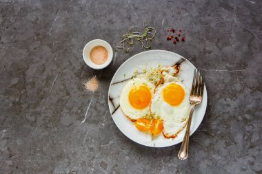 Flat-lay of breakfast fried eggs, micro greens and tomatoes in plate over grey concrete table background, top view. Clean eating, dieting, vegetarian food - Image