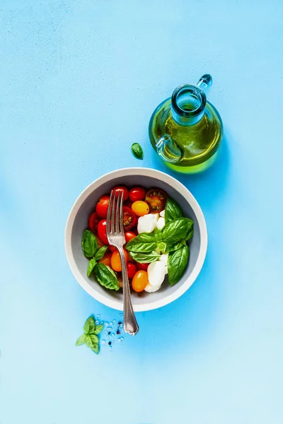 Caprese salad and ingredients on blue background flat lay. Tomato mozzarella basil leaves and olive oil. Italian cuisine. Mediterranean cuisine.