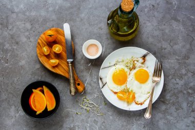 Sahanda yumurta, mikro yeşillik ve domates ile sağlıklı kahvaltı. Düz-lay plaka ve turuncu meyve gri beton tablo arka plan, üstten görünüm üzerinde kızarmış yumurta. Temiz beslenme, diyet, vejetaryen yemek - görüntü