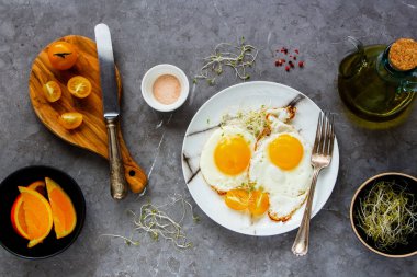 Kahvaltı kızarmış yumurta, mikro yeşillik ve domates düz yatıyordu. Plaka ve turuncu meyve gri beton tablo arka plan, üstten görünüm üzerinde kızarmış yumurta. Temiz beslenme, diyet, vejetaryen yemek - görüntü