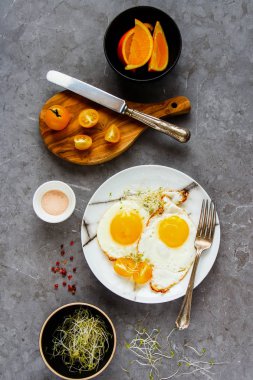 Kahvaltı Masası düz yatıyordu. Kızarmış yumurta, mikro yeşillik, domates plaka ve turuncu meyve gri beton tablo arka plan, üstten görünüm üzerinde. Temiz beslenme, diyet, vejetaryen yemek - görüntü