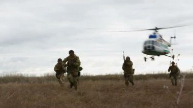 Helikopter savaş alanında askerlerin üzerinde uçar.