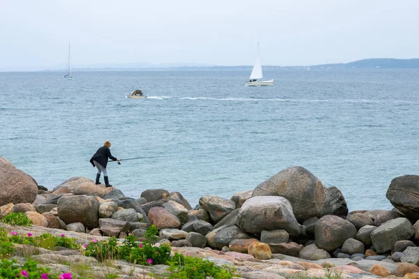 Woman is fishing on a rocky shore by the sea