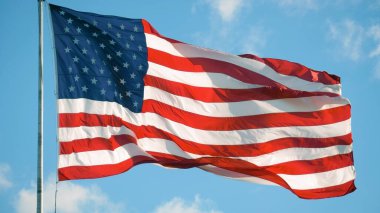 Rüzgarda dalgalanan Amerikan Bayrağı mavi bir arka planda. Amerikan Bayrağı. Mavi gökyüzünün önünde Amerika Birleşik Devletleri 'nin ünlü bayrağını sallıyordu. Anma Günü, Bağımsızlık Günü - Amerikan konsepti