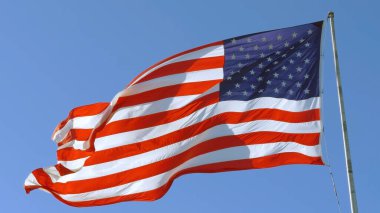 Mavi gökyüzü arka planında Amerikan bayrağı. ABD bayrağı rüzgarda dalgalanıyor. Rüzgarda dalgalanan bir Amerikan bayrağına yakın plan. Amerikan bayrağını dalgalandırın. Amerikan konsepti.