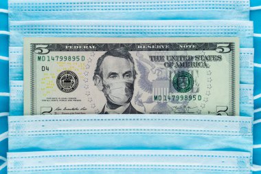 ABD 'de ilaç için maddi yardım. Amerika 'da COVID-19. Lincoln 'ün tıbbi maskeli haliyle beş dolarlık banknot. Koronavirüs sırasında ekonomiyi kurtarmak. Mavi tıbbi maskeler, ve para, üst görünüm.