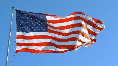 Amerikan Bayrağı mavi bir gökyüzü ile rüzgarda dalgalanıyor, Amerikan Bayrağı. Mavi gökyüzünün önünde Amerika Birleşik Devletleri 'nin ünlü bayrağını sallıyordu. Bağımsızlık Günü, İşçi Bayramı, Bayrak Günü - Amerikan Kutlaması