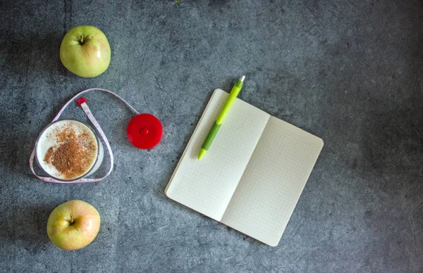 Background on the topic of weight loss - Kefir with cinnamon, an apple, a measuring tape, a notebook with a pen