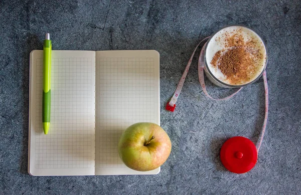Background on the topic of weight loss - Kefir with cinnamon, an apple, a measuring tape, a notebook with a pen