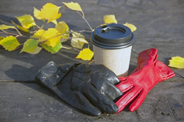 Bir bardak kahve ve iki eldiven siyah ve kırmızı sonbahar arka plan üzerinde bir ahşap arka plan üzerinde bırakır