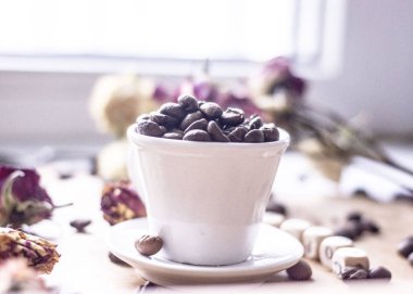 Beyaz kahve kupa kahve çekirdekleri ve kuru gül yanındaki pencerenin arka plan üzerinde kahve çekirdekleri ile