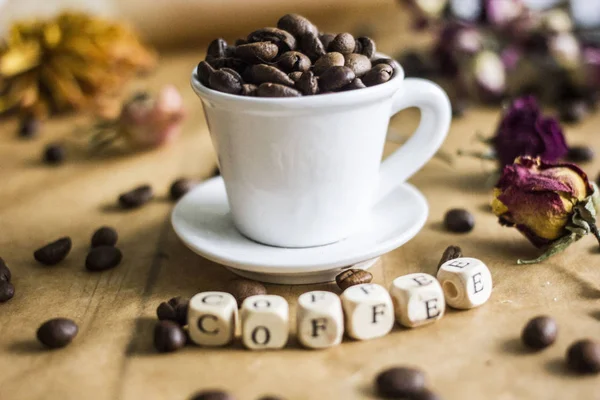White coffee mug with coffee beans on parchment paper, next to the inscription from the cubes \