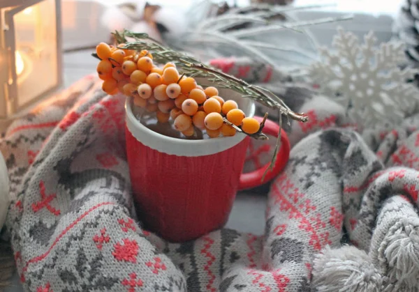 WINTER COZY BACKGROUND - RED CUP OF TEA WITH ORNAMENT, WOOL SCARF, FLASHLIGHT, KETTLE, BRANCH OF YELLOW BERRIES