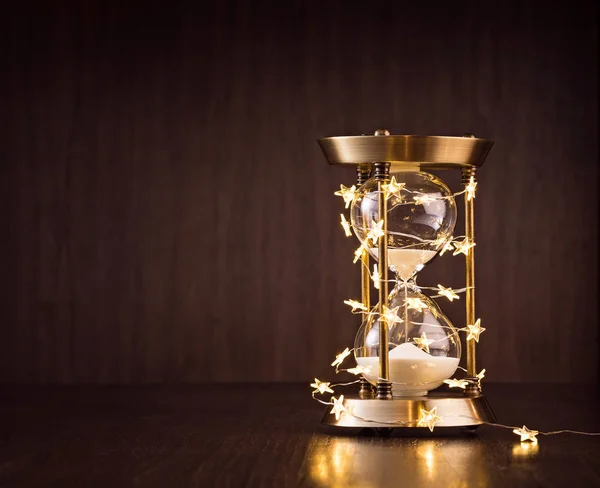 Christmas or new years countdown. Rustic Hourglass wrapped in lights with sand trickling through on a wooden background.