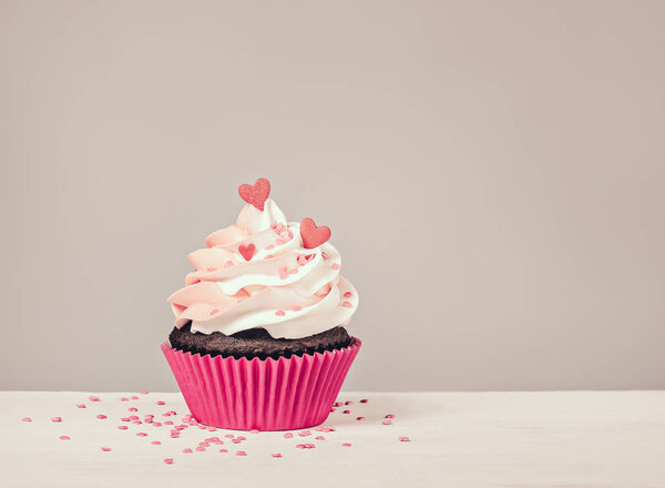 Valentines Day Cupcake treat with buttercream icing and heart sprinkles on a grey background