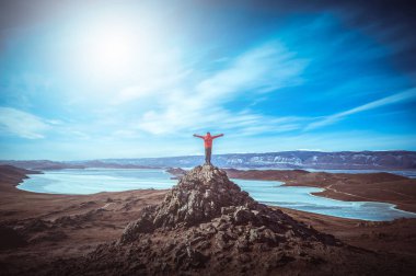 Gezgin adam kırmızı elbiseler giyer ve kolunu kaldırır Baykal Gölü yakınlarındaki dağın zirvesinde durur, Sibirya, Rusya.