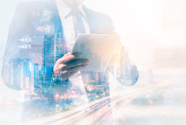 Double exposure image of businessman using digital tablet on city blurred background. Business success concept.