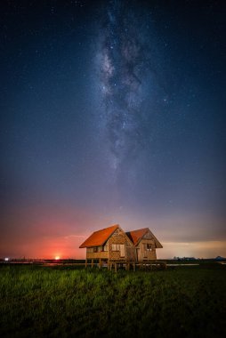 Thale Noi, Phatthalung, Tayland 'daki Chalerm Phra Kiat yolunun yakınındaki terk edilmiş ikiz evin üzerindeki samanyolu manzarası.